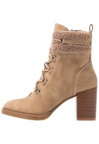 Beżowe zamszowe botki za kostkę z teksturowanym futrzanym mankietem, sznurowanym designem i brązowym słupkiem. Posiadają metalowe oczka i kontrastowe przeszycia.