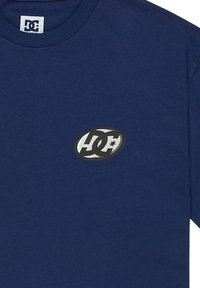 Mörkblå T-shirt i bomull, med en svartvit oval logotyp med "DC" och en stjärna. Klassisk design med rund hals.