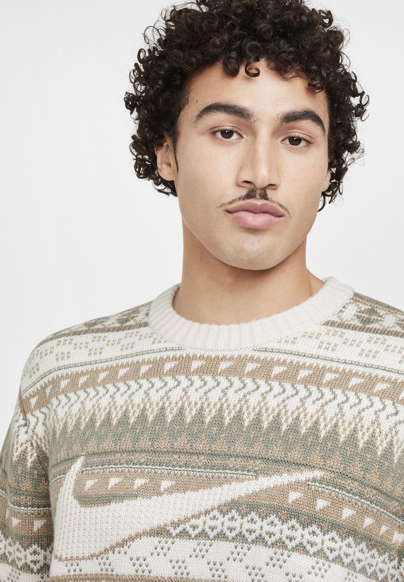 Strickpullover mit einem Muster aus Creme, Beige und Grün sowie geometrischen Designs. Gerippter Rundhalsausschnitt und strukturierter Stoff.