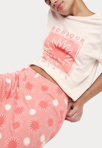 Rosa Baumwoll-T-Shirt mit "BONJOUR" und Sonnen-Motiv, kombiniert mit passenden rosa Shorts, die ein Sonnenmuster in Weiß und dunkelrosa Akzenten aufweisen.