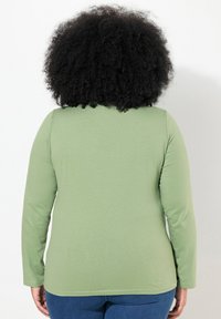 Dlouhý rukáv košile z jemné zelené látky, s jednoduchým designem a kulatým výstřihem, přiléhavými rukávy, hladkou texturou a bez vzorů.