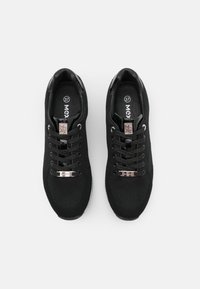 Baskets en maille noire avec une tige texturée, des éléments métalliques, des lacets plats et une semelle blanche. Étiquette de taille visible à l'intérieur.