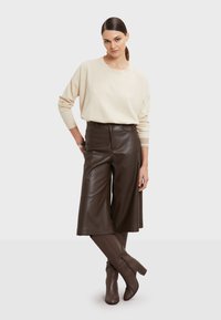 Beige oversized svetr, hnědé kalhoty z imitace kůže a hnědé kozačky na podpatku po kolena. Jednoduchý design s volným střihem a elegantní texturou.