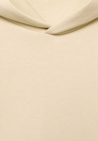Beige stof med en blød tekstur, der har en draperet halsudskæring og subtile sy detaljer, hvilket giver et glat og minimalistisk udseende.
