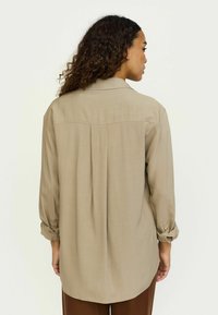 Langærmet, lysebrun skjorte med en afslappet pasform, rygdetalje og optrækkede ærmer. Glat stof med en subtil glans. Runde sømme.