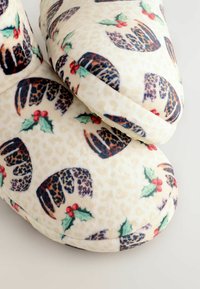 Fleece slippers i creme med et ferie mønster, der viser leopardprint og kristtornblade. Blød, rund form med holdbare såler.