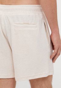 Shorts en éponge beige avec une texture douce, taille élastique, poches latérales et une petite étiquette près de la poche arrière.