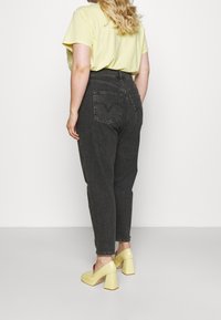 Jeans de denim negros de cintura alta con cinco bolsillos y detalles de costura, combinados con una camiseta amarilla de manga corta y zapatos de tacón amarillos.