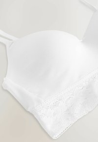 Reggiseno bianco con parte superiore in tessuto liscio, bordato da un delicato pizzo nella parte inferiore, spalline regolabili e un design senza cuciture.