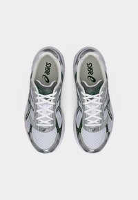 Ζευγάρι λευκών και ασημί αθλητικών παπουτσιών ASICS με πράσινες λεπτομέρειες και λευκά κορδόνια, της άποψης από πάνω σε απλό φόντο.