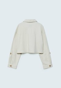 Skåret lys beige jakke med lange ærmer, knapdetaljer ved manchetterne og en klassisk krave. Blød stoftekstur med et enkelt design.