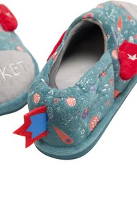 Zapatillas para niños pequeños en azul claro con patrones de cohetes, detalles en rojo y fieltro azul. Tela suave con plantillas grises y forma redondeada.
