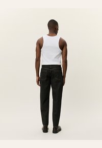 Svarte denimjeans med rett passform, med baklommer og midjebånd. Kombinert med en hvit tanktop og mørke sko.