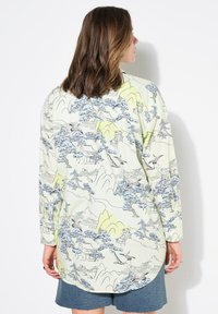 Camisa de manga larga verde claro con un estampado en estilo acuarela de montañas, árboles y edificios en tonos azules y amarillos. Con dobladillo redondeado.