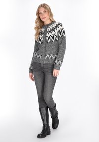 Grau gestrickte Strickjacke mit einem schwarz-weißen geometrischen Muster, runder Halsauschnitt, Knopfverschluss über die Vorderseite, kombiniert mit grauen Jeans und schwarzen knielangen Stiefeln.