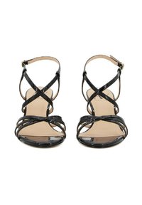Sandali in vernice nera con cinturini incrociati, punta aperta e fibbia alla caviglia. Texture liscia con una finitura lucida e soletta beige chiaro.