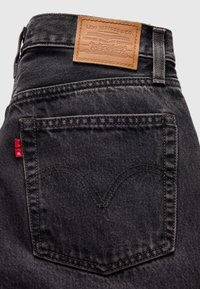 Заден джоб на черни дънки Levi's с кожена лога табелка и червен тъкан етикет, видим на страничния шев.