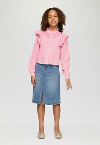 Rosa Baumwollbluse mit gerafftem Kragen und vorderen Falten, kombiniert mit einem knielangen blauen Jeansrock mit einem Schlitz vorne.