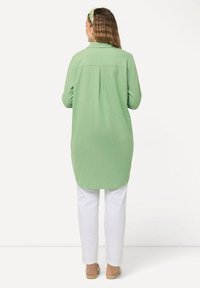 Camicia a maniche lunghe verde chiaro con colletto, caratterizzata da una piega nella parte posteriore, abbinata a pantaloni bianchi e sandali espadrilles piatti. Tessuto testurizzato.