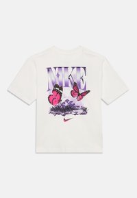 Bílé tričko s krátkým rukávem s fialovým grafickým nápisem "NIKE", růžovými motýly a detaily trávy. Zahrnuje růžové logo Nike na spodní části.