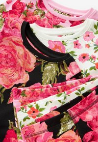 Fyra blommönstrade tygtoppar i rosa, svart och vitt, med en mjuk textur och ribbade halsar med kontrasterande färger.