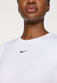 Bijela sportska majica kratkih rukava s okruglim izrezom i crnim Nike logotipom na prsima, izrađena od glatkog, rastezljivog materijala.