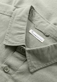 lichtgroen gestreept shirt met een omgeslagen kraag, knoopsluiting en een label met "Knowledge Cotton Apparel" in de hals.
