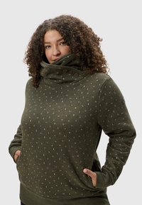 Sweatshirt vert olive avec un col haut, comportant un détail de bouton et un motif géométrique blanc sur l'ensemble. Fabriqué en tissu doux et épais.