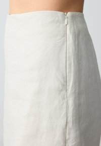 Jupe en lin beige clair à coupe droite, avec une fermeture éclair dissimulée au dos et une surface douce et texturée.