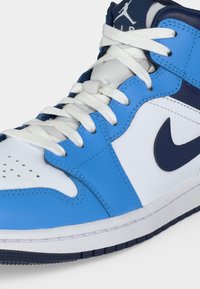 Baskets montantes blanches et bleues avec lacets blancs, swoosh Nike bleu marine et logo Jumpman sur la languette.