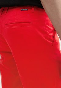 Pantalones de algodón rojos con una textura suave, que cuentan con un bolsillo trasero y una etiqueta de la marca Tom Tailor cerca de la cintura.