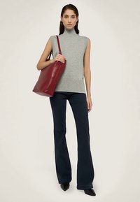 Jersey gris sin mangas con cuello alto combinado con pantalones acampanados azul oscuro. La modelo sostiene un gran bolso tote de cuero rojo intenso.