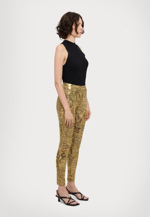 Svart ribbet ermeløs topp kombinert med gullmønstret leggings med detaljerte dyremotiver og svarte stroppehæler.