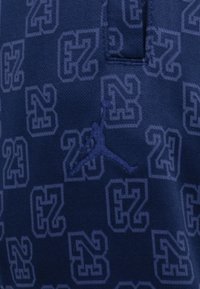Marineblåt stof med et struktureret mønster af "23" og Jumpman-logoer. Har en krave og en sidesøm for stil.