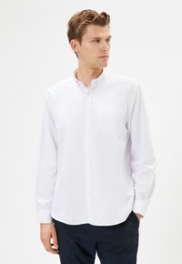 Witte langemouw blouse met een button-down kraag, een enkel borstzakje en een gladde textuur, gecombineerd met donkere broeken.