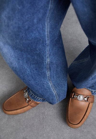 Bruna läderloafers med metalldetaljer, i kombination med löst sittande blå denimjeans med en klassisk rak ben-design.