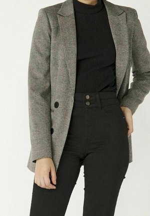 Blazer à carreaux gris avec deux boutons noirs, porté par-dessus un pull noir à côtes et un pantalon noir taille haute. Tissu lisse, design structuré.