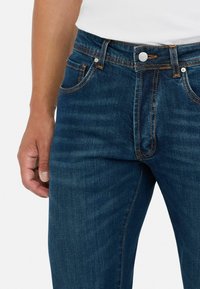 Vaqueros de denim en azul oscuro con costuras naranjas, con un corte recto, diseño estándar de cinco bolsillos y cierre de botón plateado.