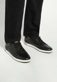 Black leather sneakers with textured sides, round toes, white rubber soles, and black laces. Detail includes a woven pattern on the sides.