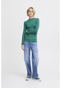 Långärmad grön topp i kombination med ljusblå raka jeans. Outfitten har en tight passform och mjuk kvalitet, med svarta sneakers.