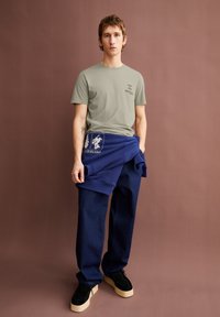 Lichtgrijs t-shirt, marineblauwe joggingbroek met grafisch, oversized ontwerp. Donkere schoenen met crème-kleurige zolen. Gladde textuur, eigentijdse pasvorm.