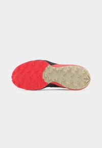 Shoe sole with red and beige rubber tread featuring angular grip patterns, designed for outdoor or trail use.