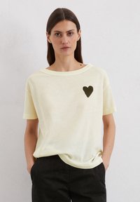 Lichtgele t-shirt met korte mouwen in zachte stof en een losse pasvorm, met een zwart hart grafiek op de linkerborst.