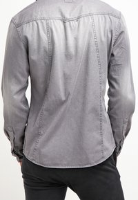 Grijze langarmshirt in een denim-achtige stof met een afgeronde zoom, een schoudernaad aan de achterkant en knoopsmanchetten, weergegeven vanuit de achteraanzicht.