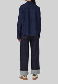 Dunkelblauses Denim-Hemd mit Button-Down-Kragen, kombiniert mit weiten dunklen Jeans mit umgeschlagenen Säumen und Sneakers mit einem beigen und schwarzen Design.