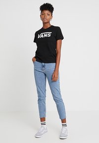 Mustat puuvillaiset t-paidat, joissa on "VANS"-logo, yhdistettyinä vaaleansinsisiin farkkuihin ja harmaisiin lenkkareihin, joissa on mustavalkoiset raidalliset sukat.