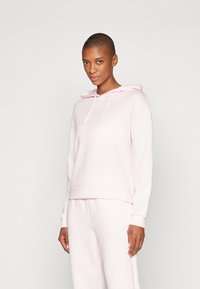 Sweatshirt rose clair avec capuche, épaules tombantes et poignets côtelés. Fabriqué en tissu doux, il présente une coupe décontractée et un minimalisme dans les détails.