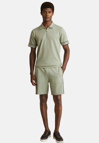 Set de cămașă polo și pantaloni scurți în verde salvie, cu accente negre pe mâneci și pantaloni. Țesătură casual cu un finisaj texturat.
