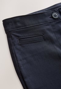 Tumši zili bikses ar gludu faktūru, ar pogas aizdari un aizmugurējo kabatu. Šuves detaļas izceļ jostasvietu.