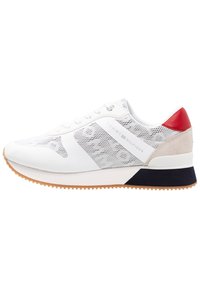 Bílé tenisky s prodyšným designem a šedými akcenty, mají červený zadní panel, béžový semišový prvek a černou patu. Texturovaná podrážka pro lepší trakci.